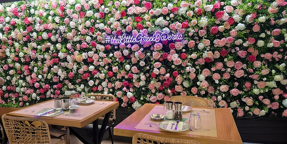 Terrasse der Little Greek Taverna mit gedeckten Tischen vor einer Blumenwand